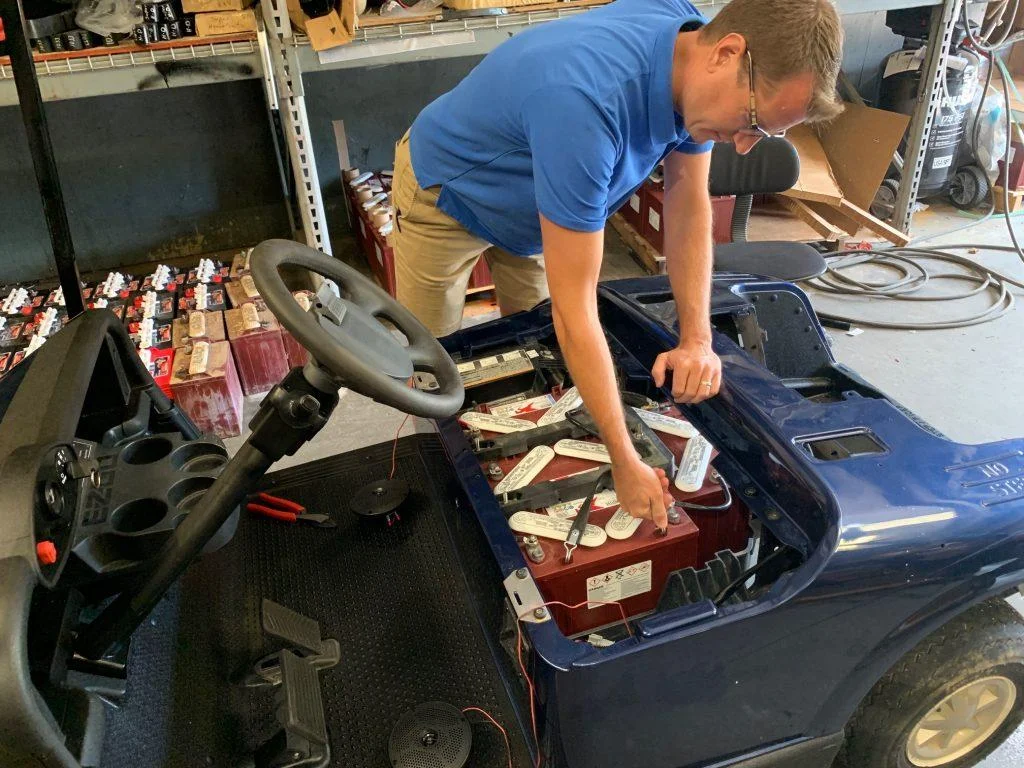 A Gold cart repair man checking the battery